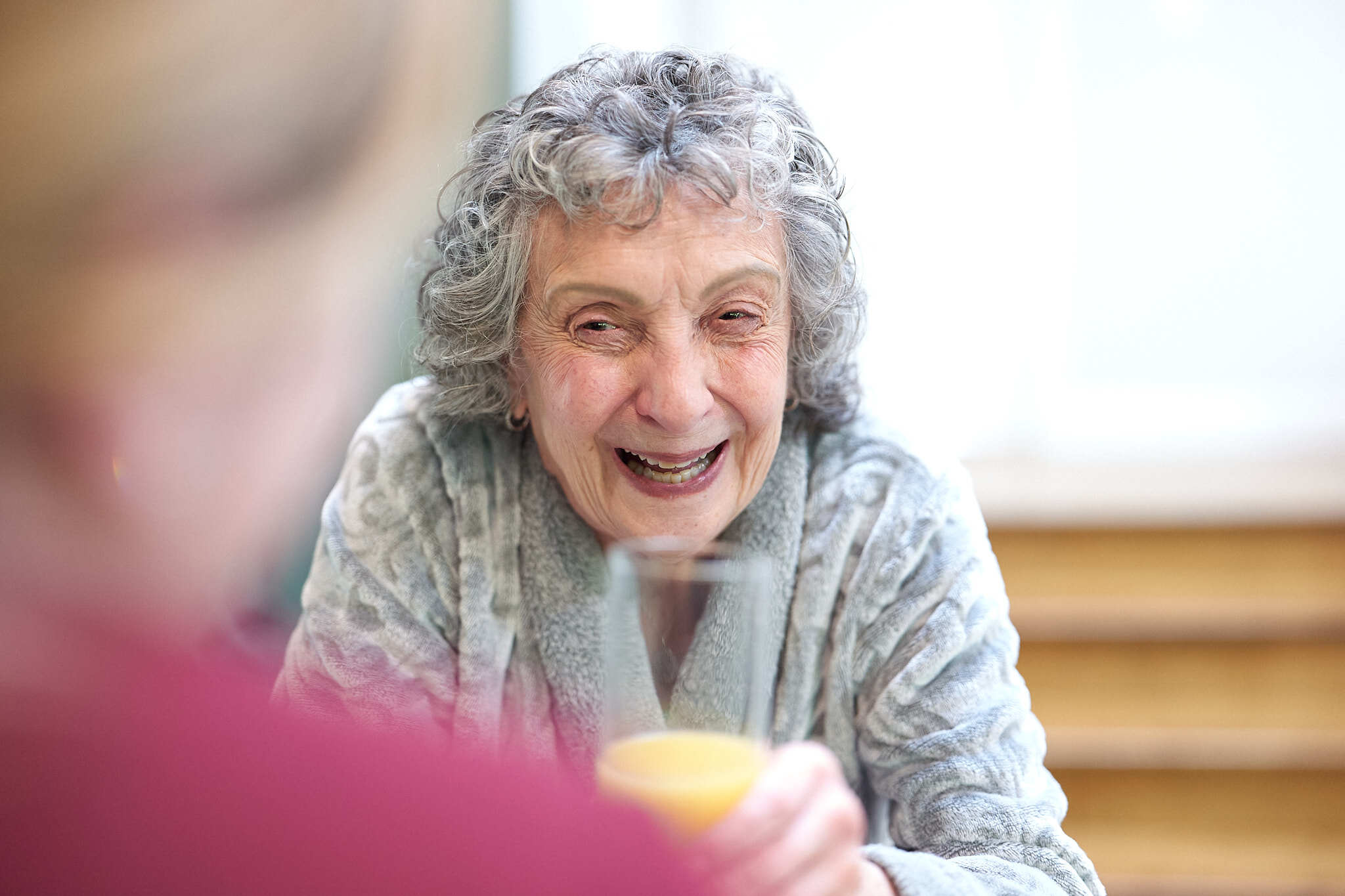 Elderly woman sipping juice and smiling.